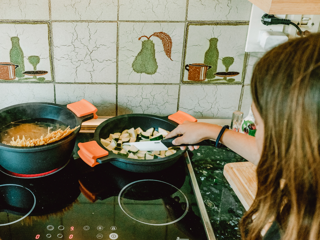 A child stirs chopped zucchini next to a pot of boiling pasta—capturing hands-on learning in kid-friendly cooking classes in Mokena, Crest Hill, and Chicago