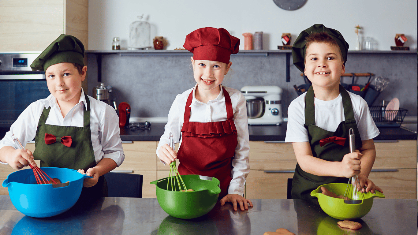 Three smiling kids in chef hats whisking batter during a hands-on baking class at Farmhouse Academy near Lockport, Plainfield, and Homer Glen, Illinois