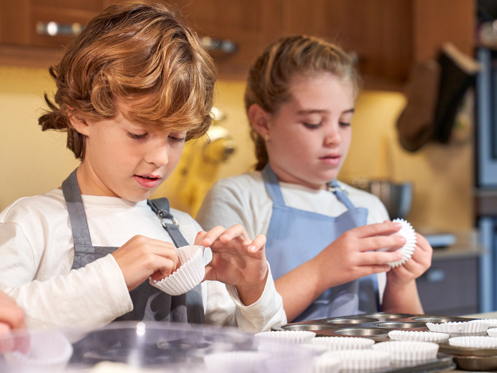 Two kids prepare cupcake liners in a baking class—hands-on culinary fun in Mokena, Crest Hill, and Chicago that teaches confidence and kitchen skills