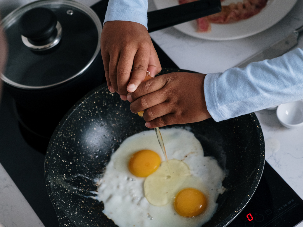 A child cracks eggs into a skillet during a fun and educational kids' cooking class in Mokena, Crest Hill, or Chicago—perfect hands-on experience for young chefs learning to make breakfast