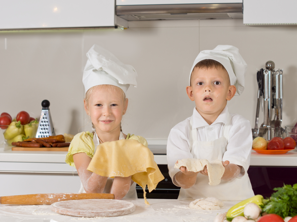 Two smiling young chefs in training roll out dough during a fun kids’ cooking class in Chicago, Crest Hill, or Mokena. A hands-on kitchen experience for budding bakers and chefs