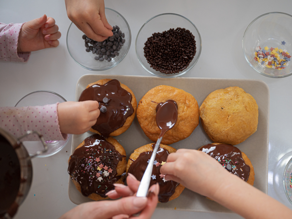 Children decorating chocolate-covered donuts with sprinkles and toppings during a fun hands-on baking class at Farmhouse Academy near Frankfort, Mokena, and New Lenox, Illinois