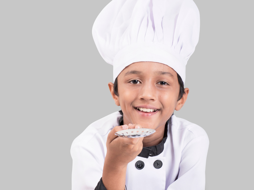 A happy young chef in a tall white hat samples a creation with pride—perfectly capturing the excitement of kids’ culinary classes in Mokena, Crest Hill, and the greater Chicago area.