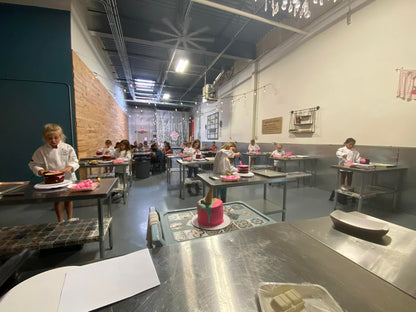 Children decorating cakes in a hands-on baking class at Farmhouse Academy’s kitchen classroom in Mokena, Illinois, with family and friends observing in the background