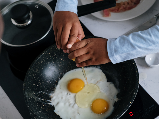 A child cracks eggs into a skillet during a fun and educational kids' cooking class in Mokena, Crest Hill, or Chicago—perfect hands-on experience for young chefs learning to make breakfast