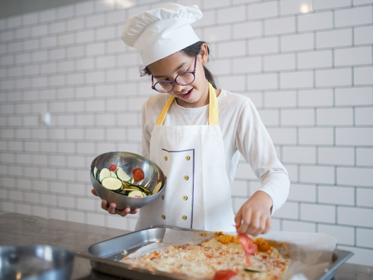 Young chef adds fresh veggies to homemade pizza at a fun and engaging kids' cooking class near Chicago, Crest Hill, and Mokena—where culinary creativity starts early