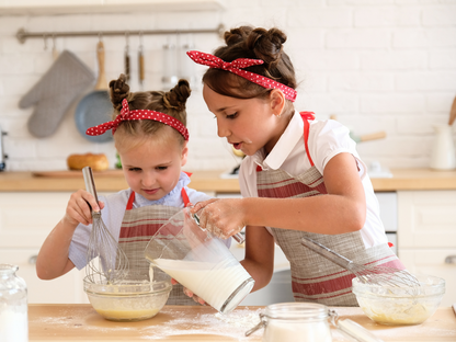 Two young girls in aprons baking together, pouring milk and whisking batter in a kids' baking class in Chicago, Crest Hill, or Mokena.